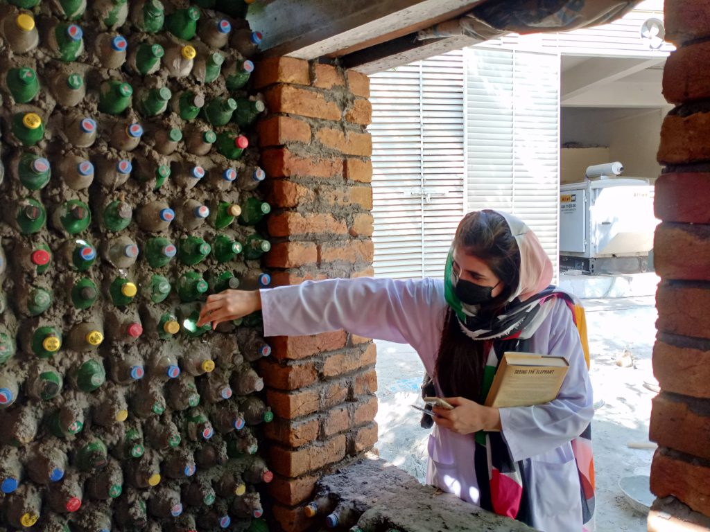 A woman points at a wall built from plastic bottles packed with waste.
