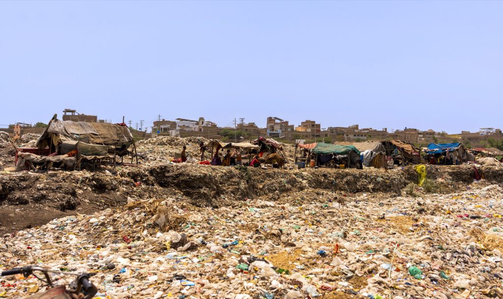 A wide view of an open dumpsite with waste spread across the ground under a clear sky.